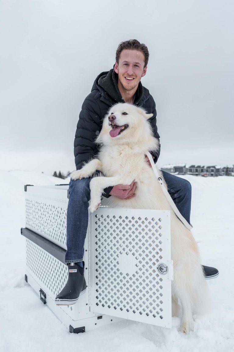Man with Husky on a durable dog crate in snowy winter setting.